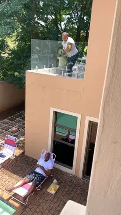 Woman dumps a full bucket of water on her husband from the balcony above him