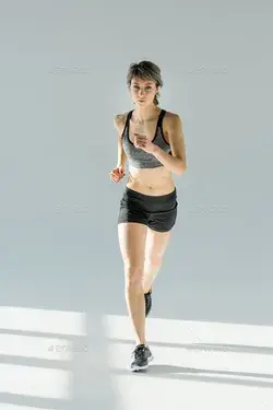 front view of running woman in sportive clothing on grey Stock Photo by LightFieldStudios