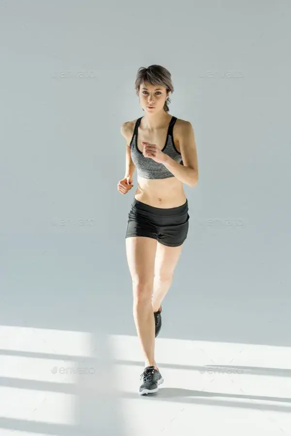 front view of running woman in sportive clothing on grey Stock Photo by LightFieldStudios